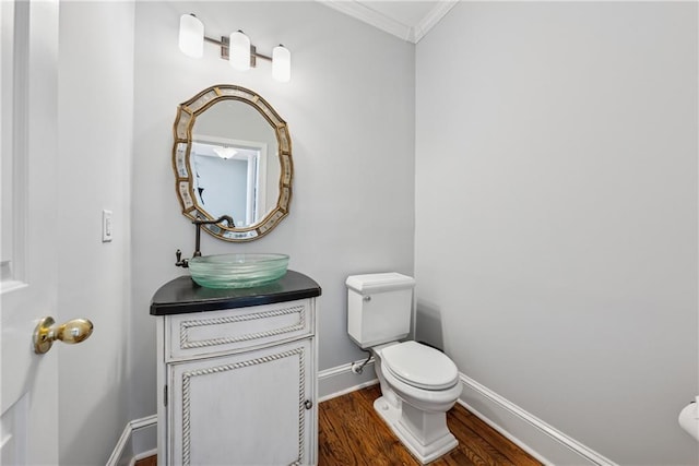 half bathroom with toilet, ornamental molding, vanity, wood finished floors, and baseboards