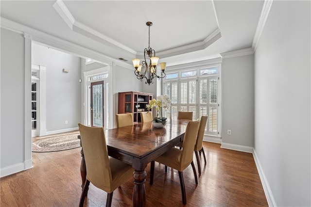 dining space with crown molding, a tray ceiling, wood finished floors, and baseboards