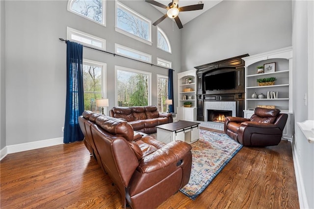 living area featuring a fireplace, a high ceiling, a ceiling fan, wood finished floors, and baseboards