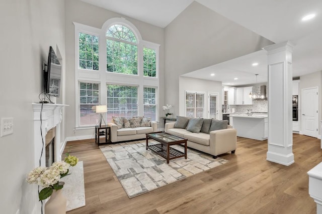 1547 Trilogy Park, Hoschton, GA 30548 - living area featuring light wood-style flooring, a towering ceiling, a fireplace with flush hearth, ornate columns, and baseboards