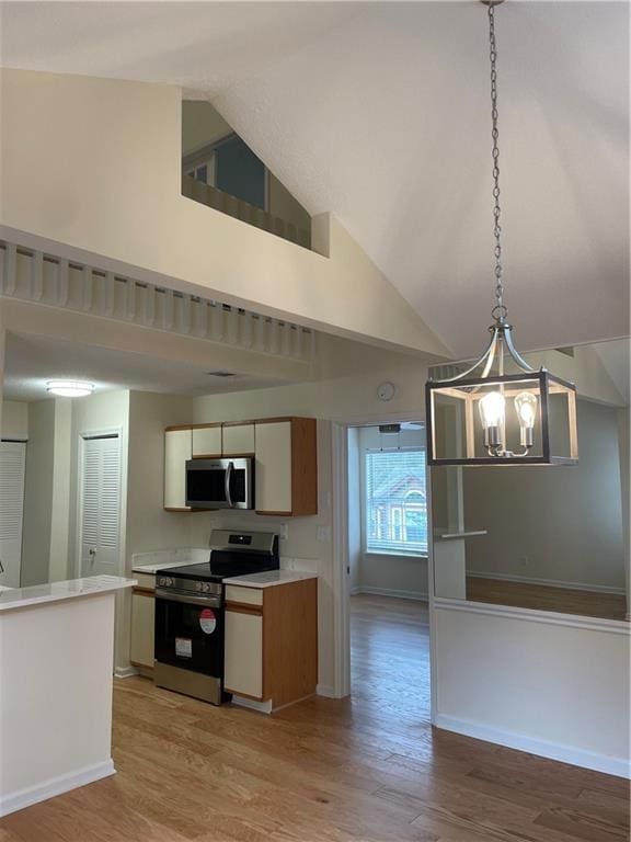 kitchen with pendant lighting, light wood-style floors, high vaulted ceiling, light countertops, and appliances with stainless steel finishes