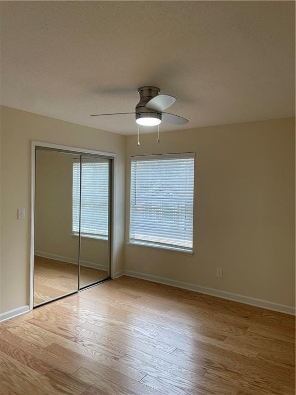 unfurnished bedroom with ceiling fan, a textured ceiling, baseboards, a closet, and light wood-type flooring