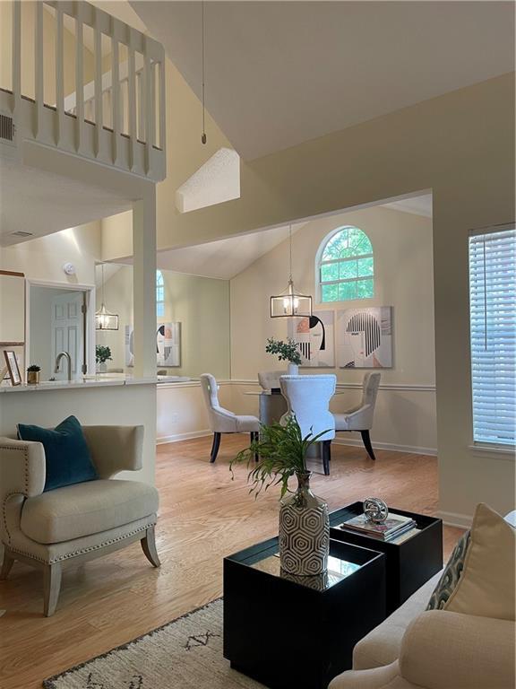 living area with baseboards, wood finished floors, a chandelier, and high vaulted ceiling