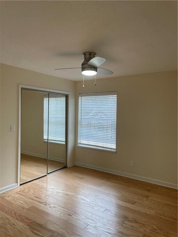 unfurnished bedroom featuring baseboards, a ceiling fan, a closet, and light wood-type flooring