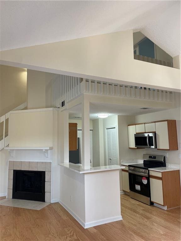 kitchen with high vaulted ceiling, stainless steel appliances, light countertops, light wood finished floors, and a tiled fireplace