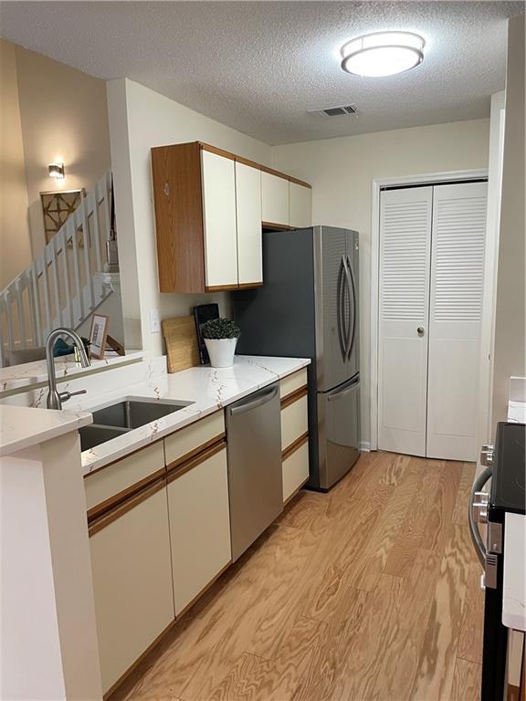 kitchen with a textured ceiling, stainless steel dishwasher, a sink, light countertops, and light wood-style flooring
