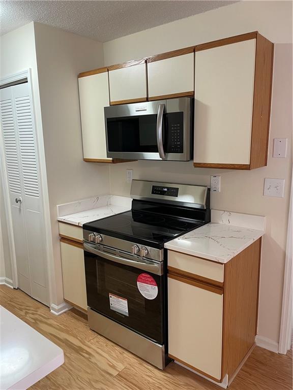 kitchen with a textured ceiling, white cabinetry, baseboards, light wood-style floors, and appliances with stainless steel finishes