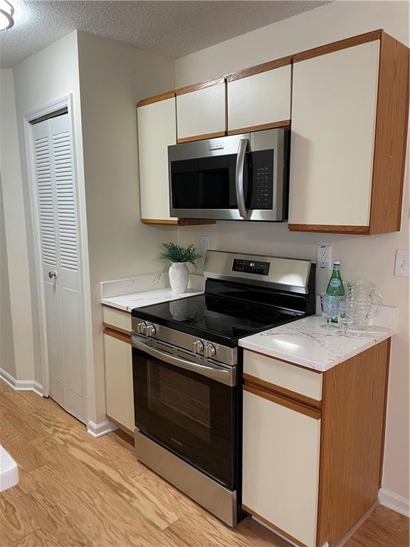 kitchen with baseboards, white cabinets, stainless steel appliances, and light wood finished floors