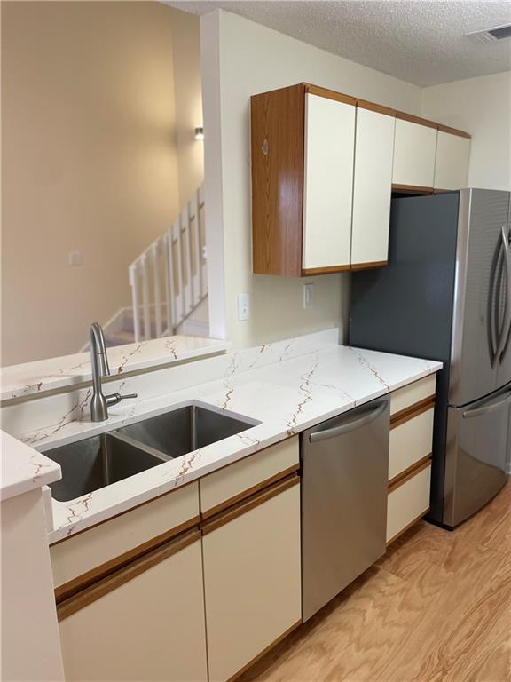 kitchen featuring a textured ceiling, stainless steel appliances, a sink, white cabinets, and light stone countertops