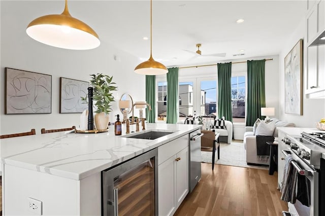 kitchen featuring sink, high end stainless steel range, white cabinets, wine cooler, and hanging light fixtures