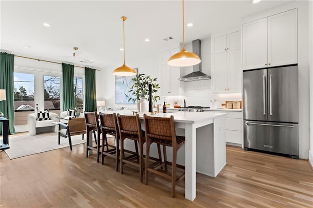 kitchen featuring french doors, wall chimney range hood, a center island with sink, white cabinets, and stainless steel refrigerator