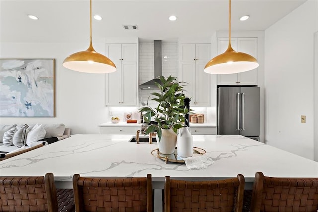 kitchen featuring pendant lighting, white cabinets, wall chimney range hood, high quality fridge, and a large island