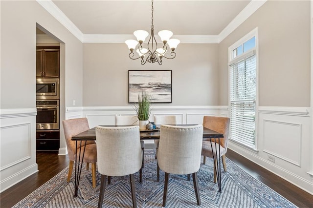 dining room with a wainscoted wall, dark wood finished floors, a decorative wall, ornamental molding, and a chandelier