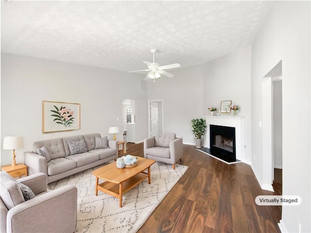 living area with lofted ceiling, a fireplace with raised hearth, wood finished floors, and a textured ceiling