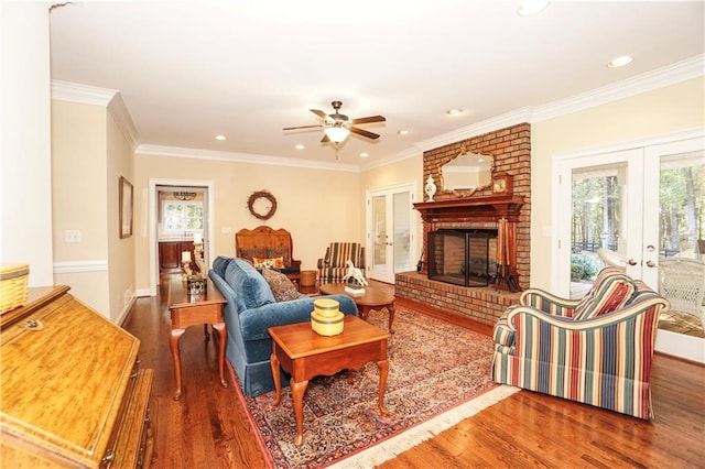 living room with ceiling fan, french doors, dark wood-type flooring, a brick fireplace, and crown molding