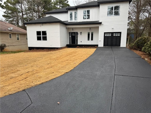 modern inspired farmhouse with an attached garage, driveway, a front lawn, and board and batten siding