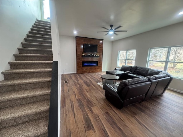 living room featuring a large fireplace, baseboards, ceiling fan, stairway, and dark wood-type flooring