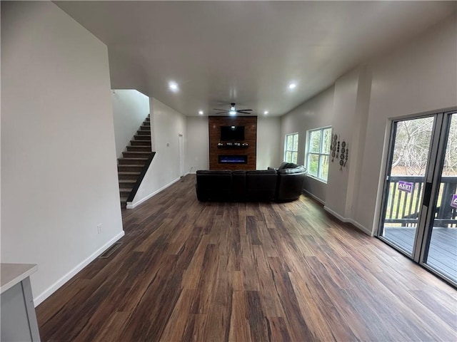 unfurnished living room featuring dark wood-type flooring, stairway, and baseboards