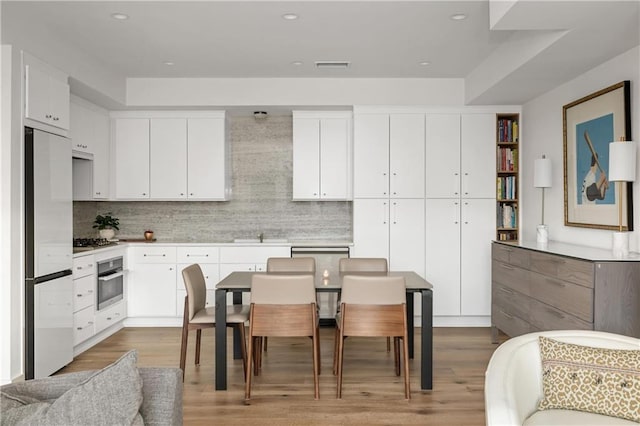 kitchen featuring white cabinets, light wood-type flooring, stainless steel appliances, and tasteful backsplash