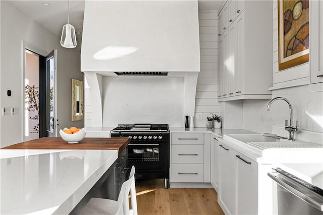 kitchen featuring pendant lighting, black gas stove, sink, light hardwood / wood-style flooring, and white cabinetry