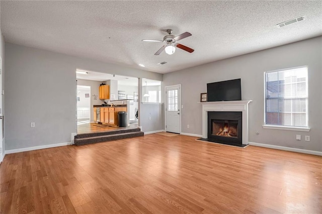 unfurnished living room with a textured ceiling, light hardwood / wood-style floors, and ceiling fan