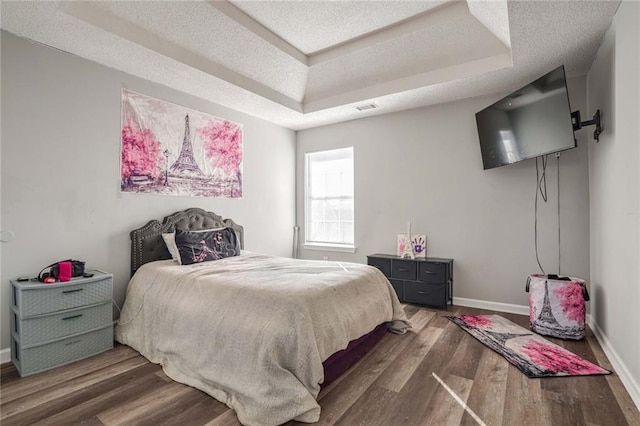 bedroom with dark wood-type flooring, a textured ceiling, and a tray ceiling