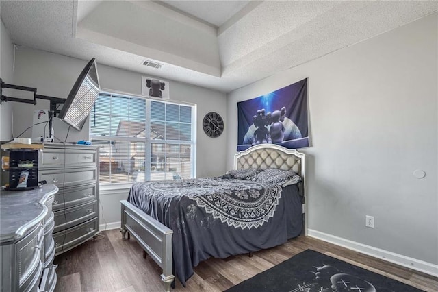 bedroom with dark wood-type flooring, a raised ceiling, and a textured ceiling