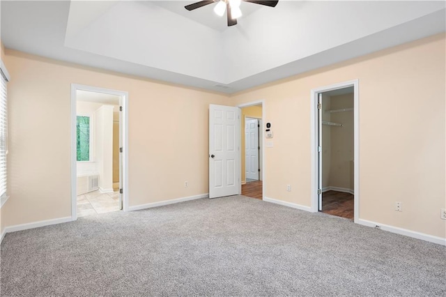 unfurnished bedroom featuring carpet floors, baseboards, a raised ceiling, a spacious closet, and ensuite bathroom