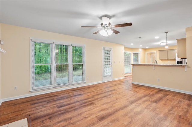 unfurnished living room with light wood-style floors, baseboards, and ceiling fan