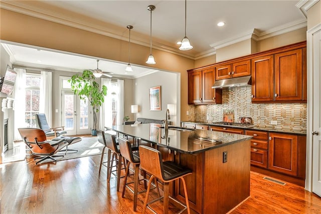 kitchen featuring sink, stainless steel gas stovetop, backsplash, hanging light fixtures, and a kitchen island with sink