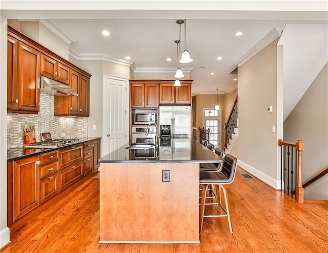 kitchen with hanging light fixtures, stainless steel appliances, a center island with sink, tasteful backsplash, and sink