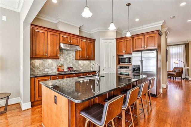 kitchen featuring decorative light fixtures, stainless steel appliances, tasteful backsplash, a kitchen island with sink, and sink