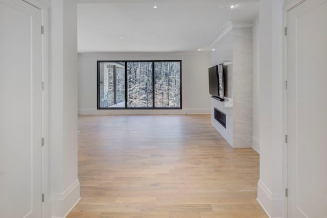 unfurnished living room with a large fireplace, crown molding, baseboards, and light wood-style floors