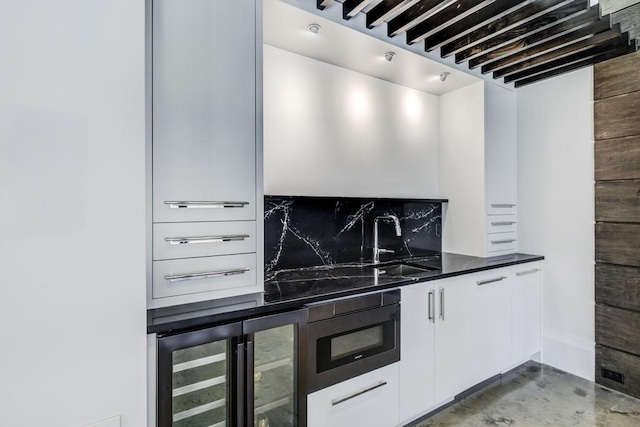 kitchen with tasteful backsplash, white cabinets, a sink, beverage cooler, and baseboards