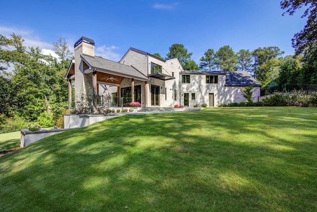 rear view of property with a chimney, brick siding, a patio, a ceiling fan, and a lawn