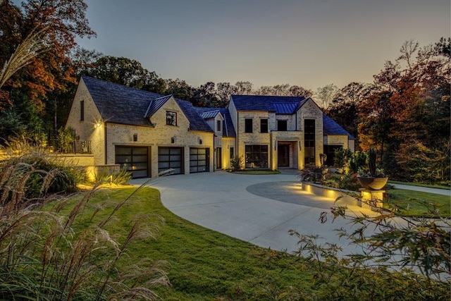 french country home featuring an attached garage, stone siding, concrete driveway, a lawn, and a standing seam roof