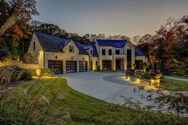 french country home featuring a high end roof, concrete driveway, stone siding, a yard, and a garage