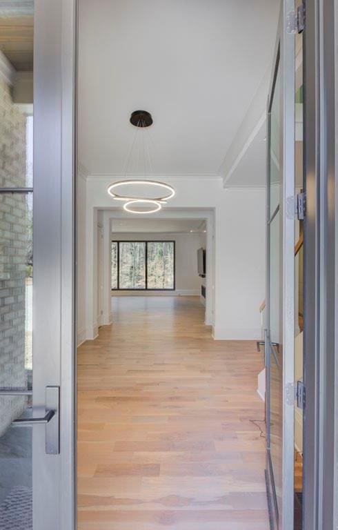 hallway with baseboards, ornamental molding, stairs, light wood-type flooring, and a chandelier