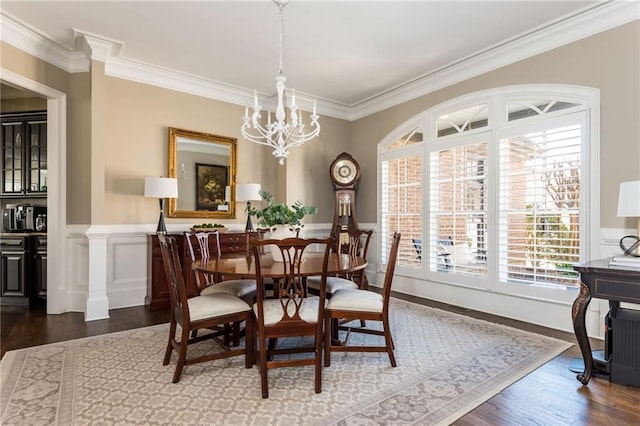 dining area with a wainscoted wall, ornamental molding, wood finished floors, and a notable chandelier