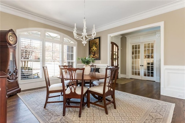 dining room featuring french doors, dark wood finished floors, a notable chandelier, crown molding, and wainscoting