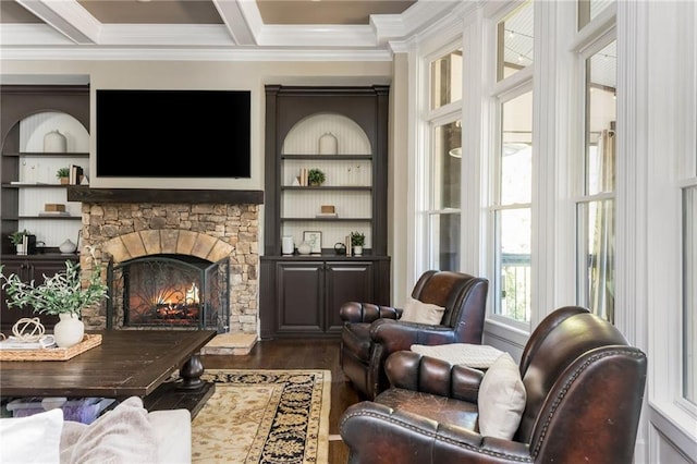 living area featuring ornamental molding, beamed ceiling, wood finished floors, and a stone fireplace