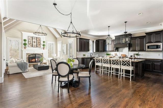 dining space with a chandelier, lofted ceiling, a fireplace, ornamental molding, and dark wood finished floors