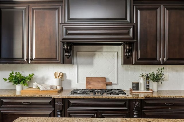 kitchen with dark brown cabinets, tasteful backsplash, light stone countertops, and stainless steel gas stovetop