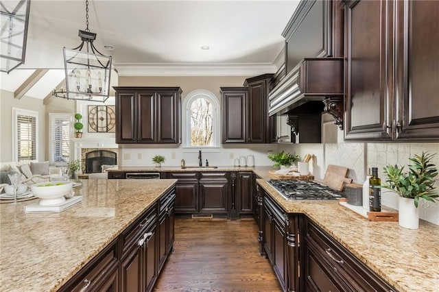 kitchen with decorative backsplash, light stone counters, hanging light fixtures, stainless steel gas stovetop, and a sink