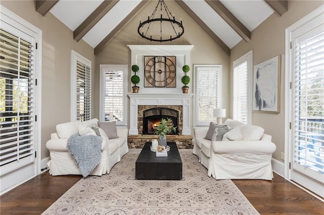 living area with a stone fireplace, wood finished floors, beam ceiling, and a healthy amount of sunlight