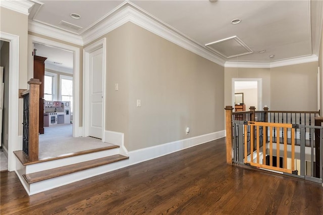 hallway with dark wood-style flooring, an upstairs landing, attic access, and crown molding