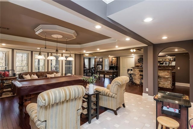 living room with arched walkways, a tray ceiling, visible vents, and crown molding