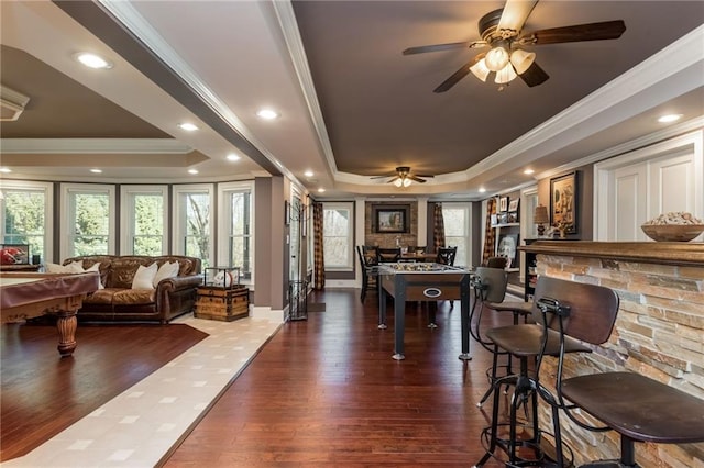 rec room featuring dark wood-style floors, a raised ceiling, crown molding, and a fireplace