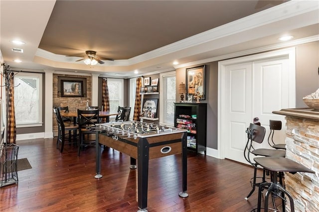 recreation room with ceiling fan, dark wood-style flooring, baseboards, ornamental molding, and a raised ceiling