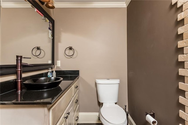 half bathroom with baseboards, vanity, toilet, and crown molding